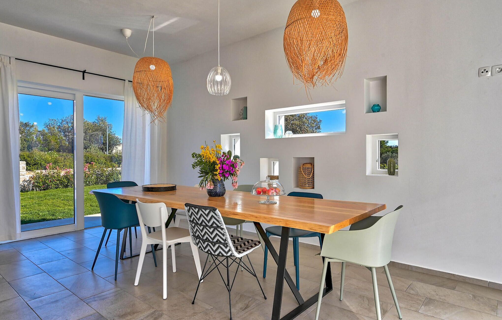 A modern dining area with a wooden table, white and blue chairs, and decorative hanging lights.