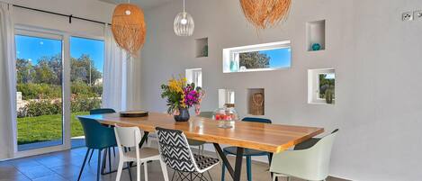 A modern dining area with a wooden table, white and blue chairs, and decorative hanging lights.