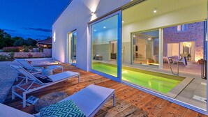 Un espace piscine extérieur moderne, doté de chaises longues et d’une terrasse en bois.