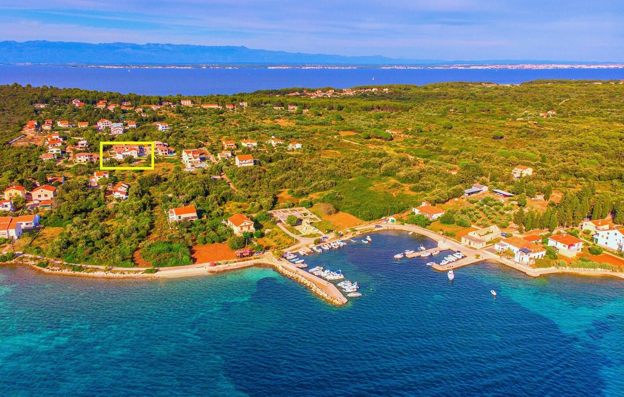 An aerial view of a coastal village with houses, a marina, and clear blue waters.