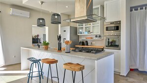 Une cuisine moderne dotée d’un îlot central, de tabourets de bar, d’une cuisinière et d’appareils électroménagers intégrés.