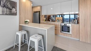 A modern kitchen with a central island, white bar stools, and a view of the city. - City Living! 1Bed/1Bath/Pool (Brisbane City)