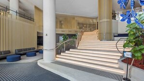 A modern lobby with a staircase, seating areas, and a vertical wooden panel wall. - City Living! 1Bed/1Bath/Pool (Brisbane City)