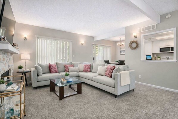 A living room with a sectional sofa, a glass coffee table, and a fireplace.