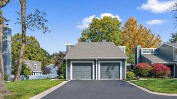 A two-story residential building with a garage, surrounded by trees and a well-maintained lawn.