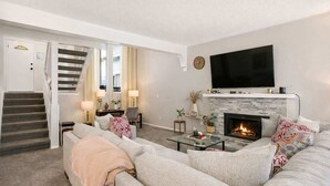 Una sala de estar con chimenea, un televisor de pantalla plana y una escalera que lleva a otra habitación.