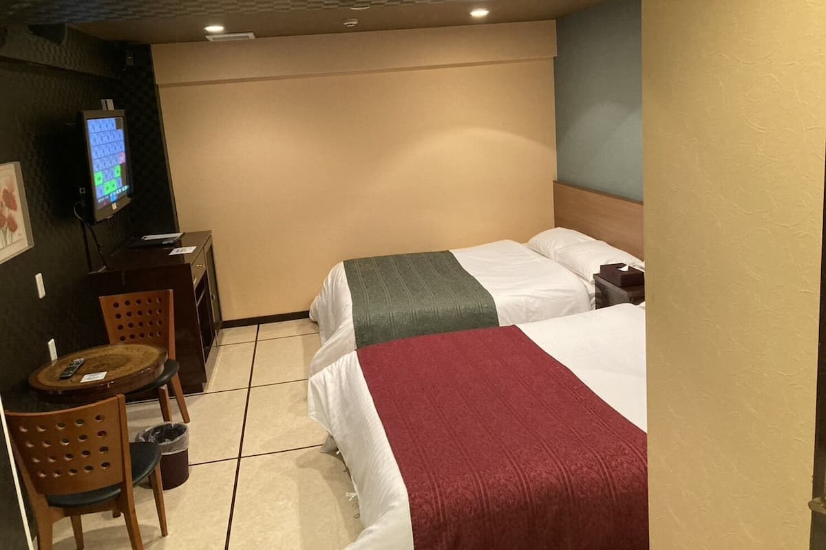 A hotel room with two beds, a desk with a chair, a television, and a small trash bin.