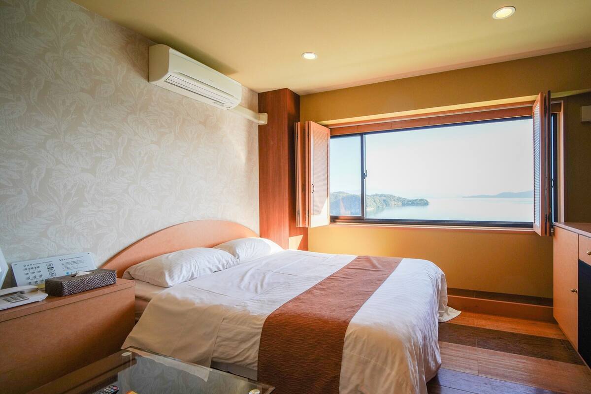 Quarto de hotel com cama, mesa de cabeceira, ar condicionado, janela com vista e televisão.