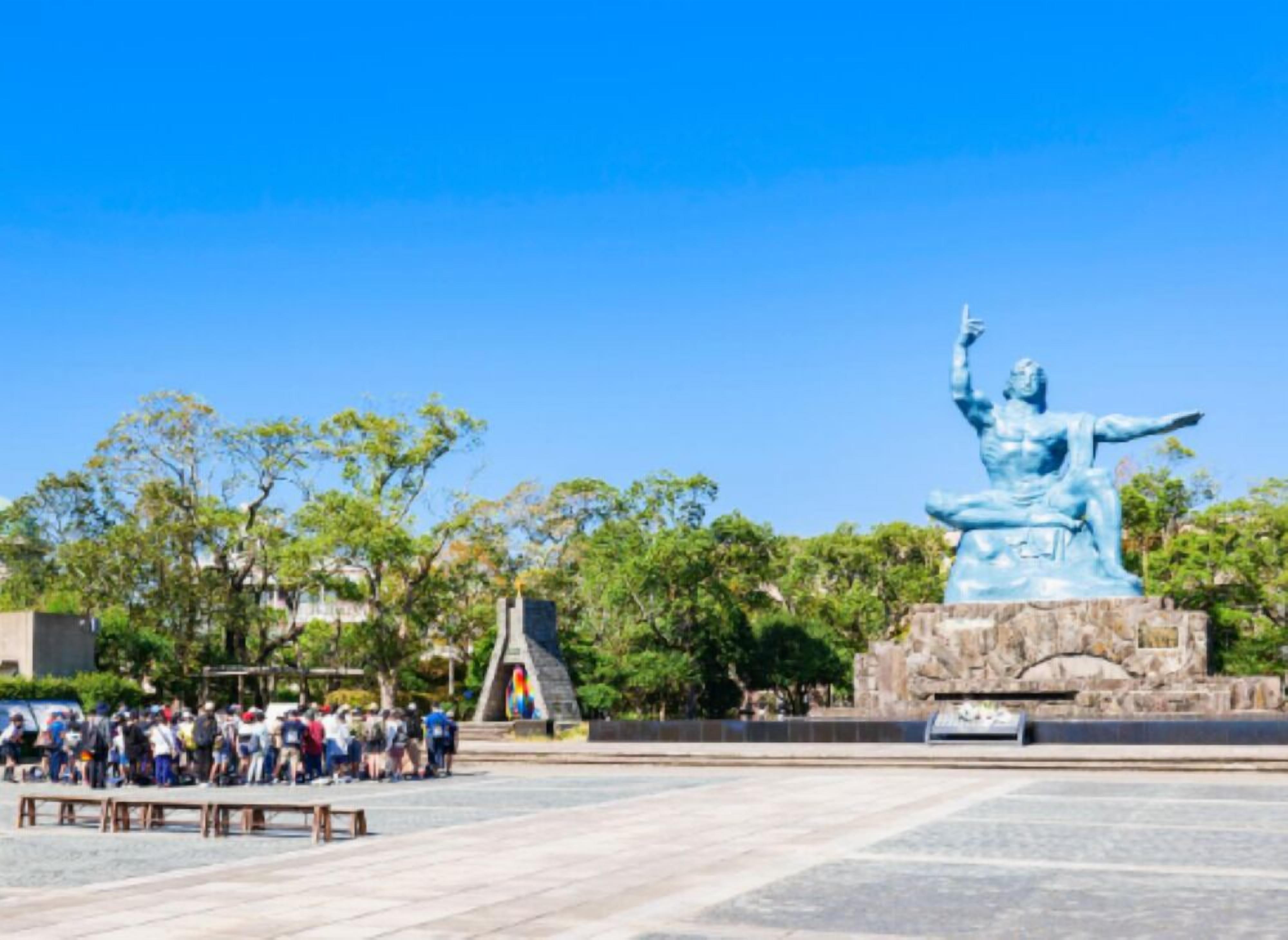 Una estatua azul grande en una plaza pública, con bancos y árboles alrededor.