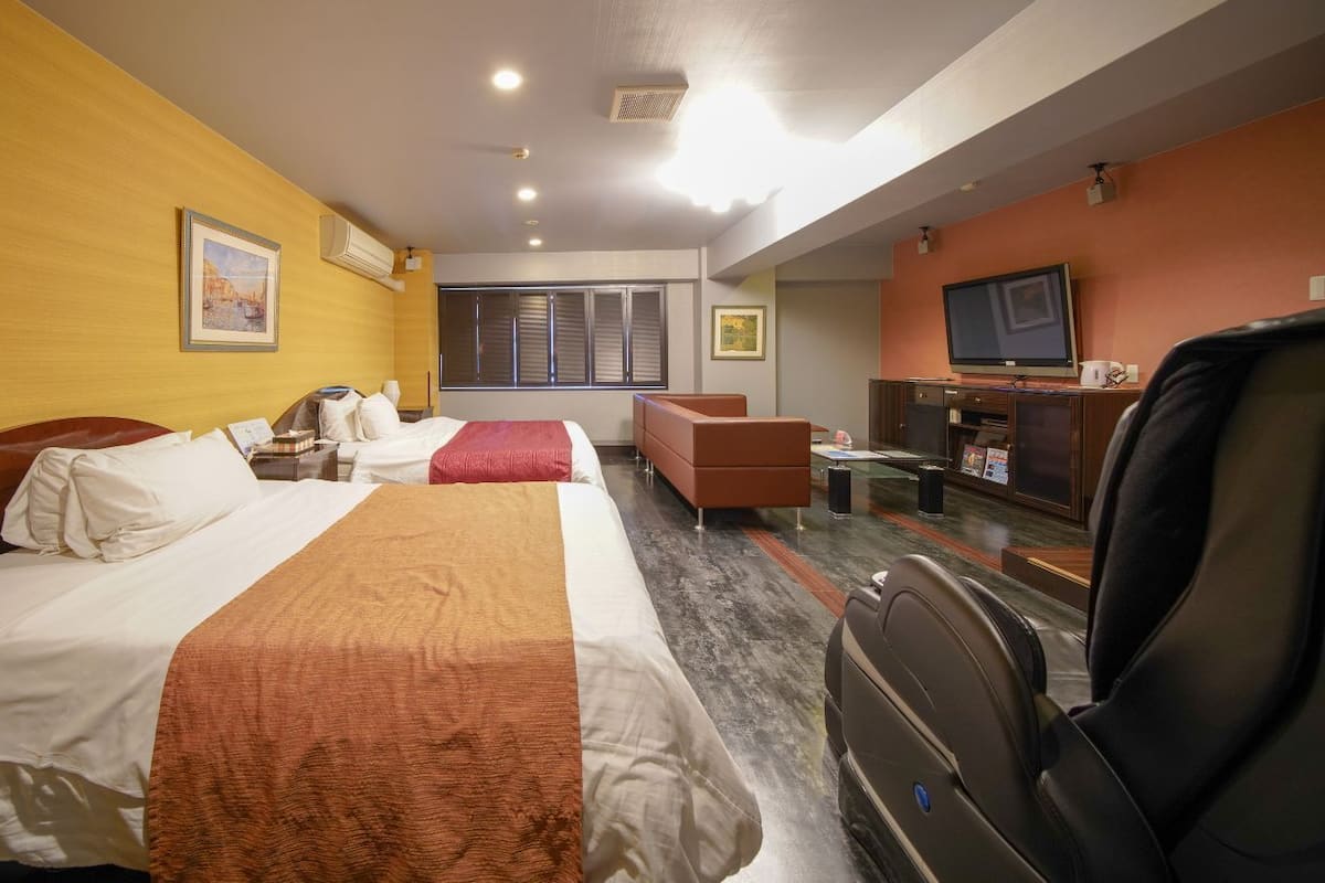 Quarto de hotel com duas camas, um sofá, uma TV e uma mesa de escritório com um computador.