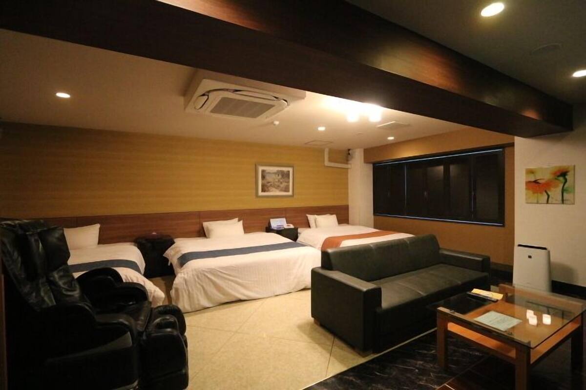 Quarto de hotel com duas camas, um sofá, uma poltrona de massagem e uma pequena mesa.