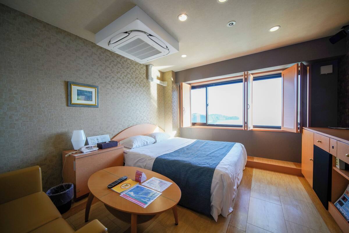 Quarto de hotel com cama, escrivaninha, cadeira, mesa, televisão e janela com vista.
