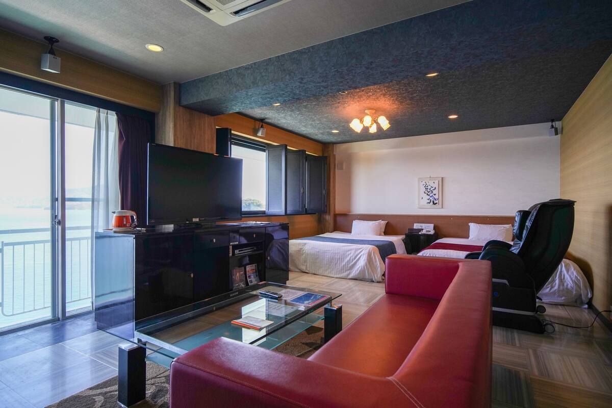 Quarto de hotel moderno com uma televisão de tela plana grande, um sofá, uma cama, uma poltrona de massagem e uma mesa de centro de vidro.
