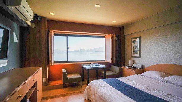 A hotel room with a bed, a desk, a chair, a window with a view, and an air conditioning unit. - HOTEL LAVIEN (Togitsu)