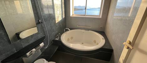 A bathroom with a large bathtub, a mirror, and a window with a view of the sea.