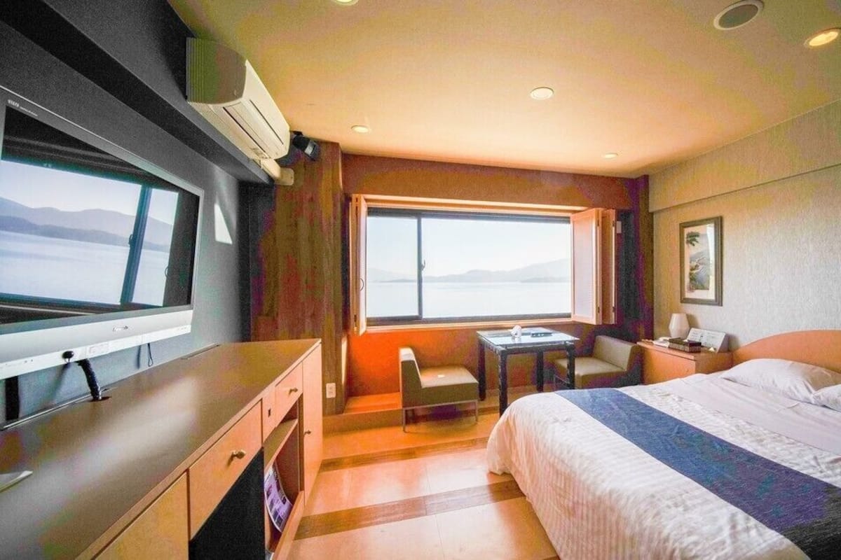 A hotel room with a bed, a desk, a chair, a TV, and a window with a view.