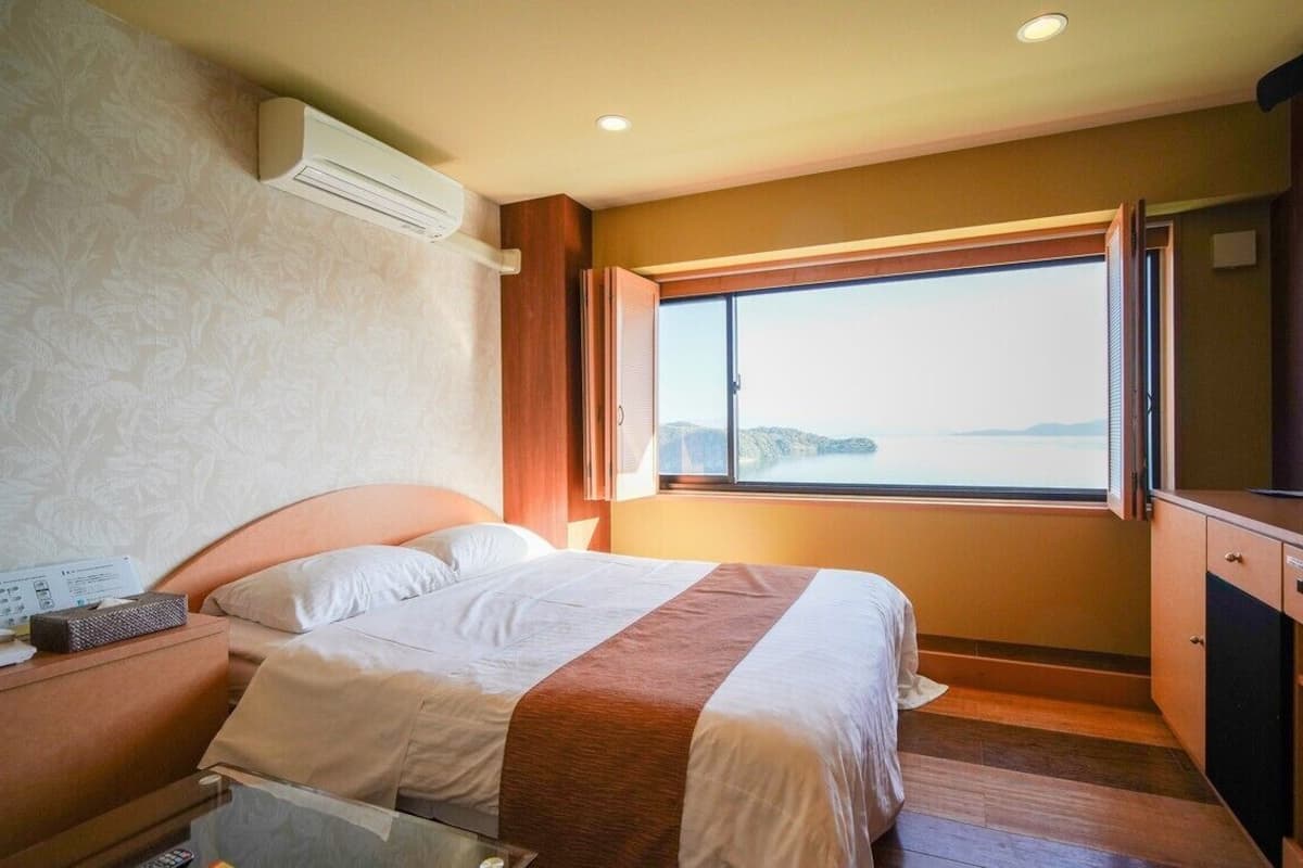 A hotel room with a bed, a desk, a television, and a window with a view of the sea.