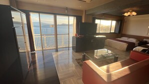 A hotel room with a balcony, a glass coffee table, a sofa, a TV, and a bed with pillows. - HOTEL LAVIEN (Togitsu)