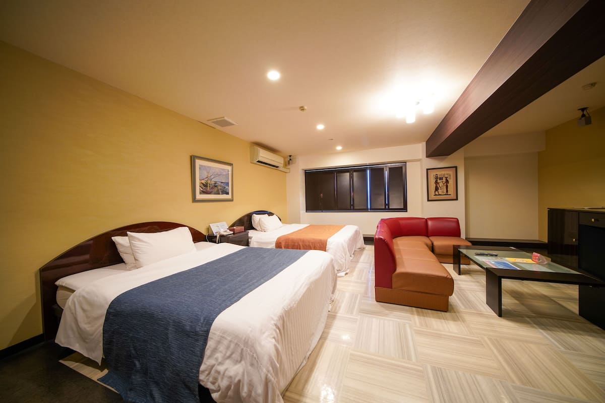 Quarto de hotel com duas camas, um sofá, uma televisão e uma janela.
