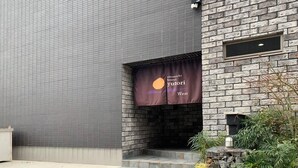 A building with a grey tiled exterior and a stone facade. There is a banner with the text "anomichi hostel yutori West" hanging from the stone facade. - Yutori (Onomichi)