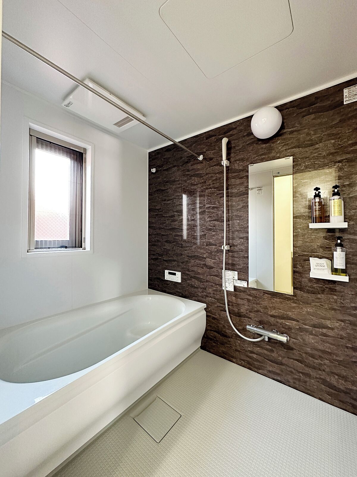 A modern bathroom with a large bathtub, a shower, a mirror, and a window.