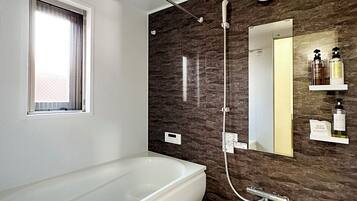 A modern bathroom with a large bathtub, a shower, a mirror, and a window.