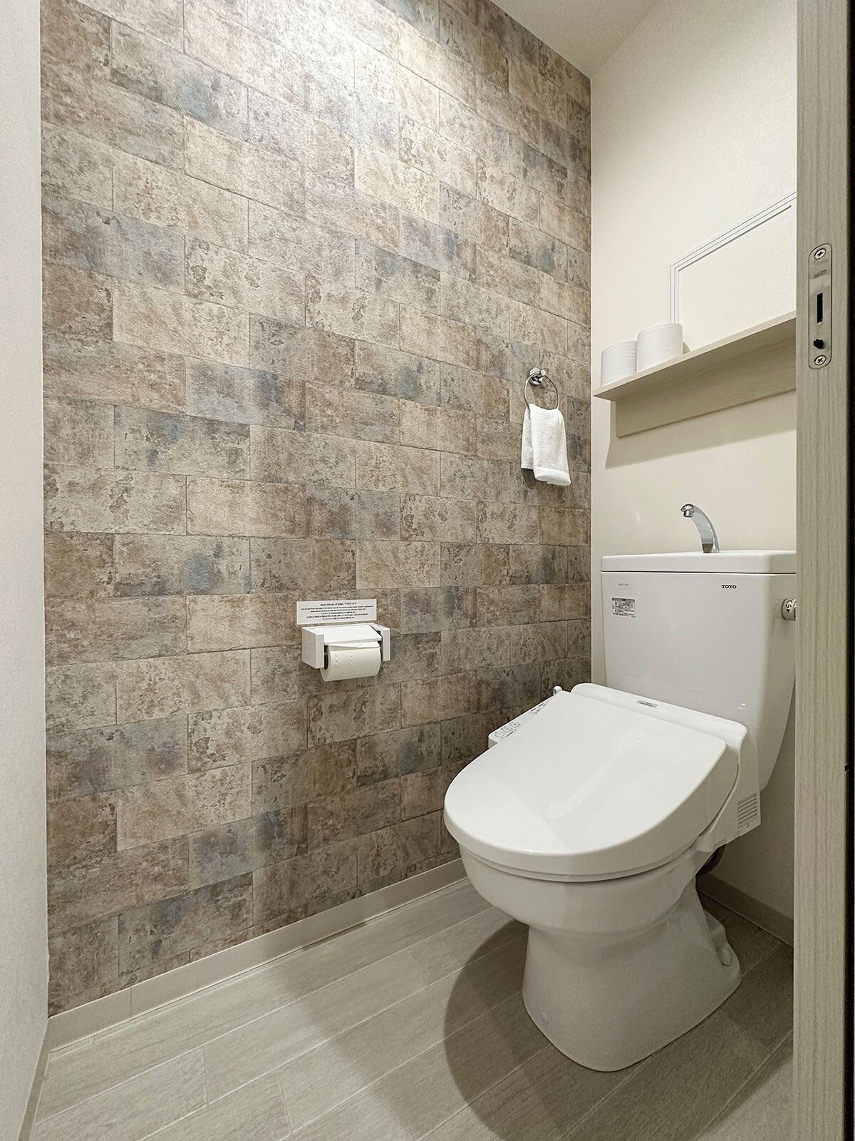 Un baño con pared de piedra, inodoro, lavamanos y toallero.