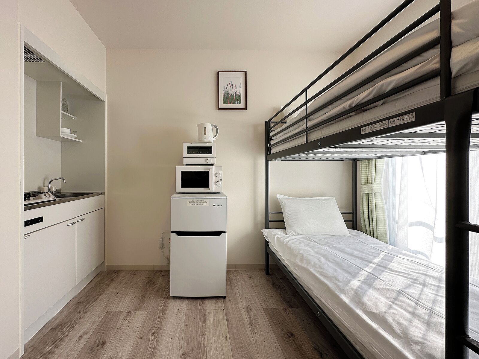 Una habitación compacta con una cama litera, un kitchenette con microondas y un mueble pequeño.
