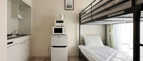 Una habitación compacta con una cama litera, un kitchenette con microondas y un mueble pequeño.