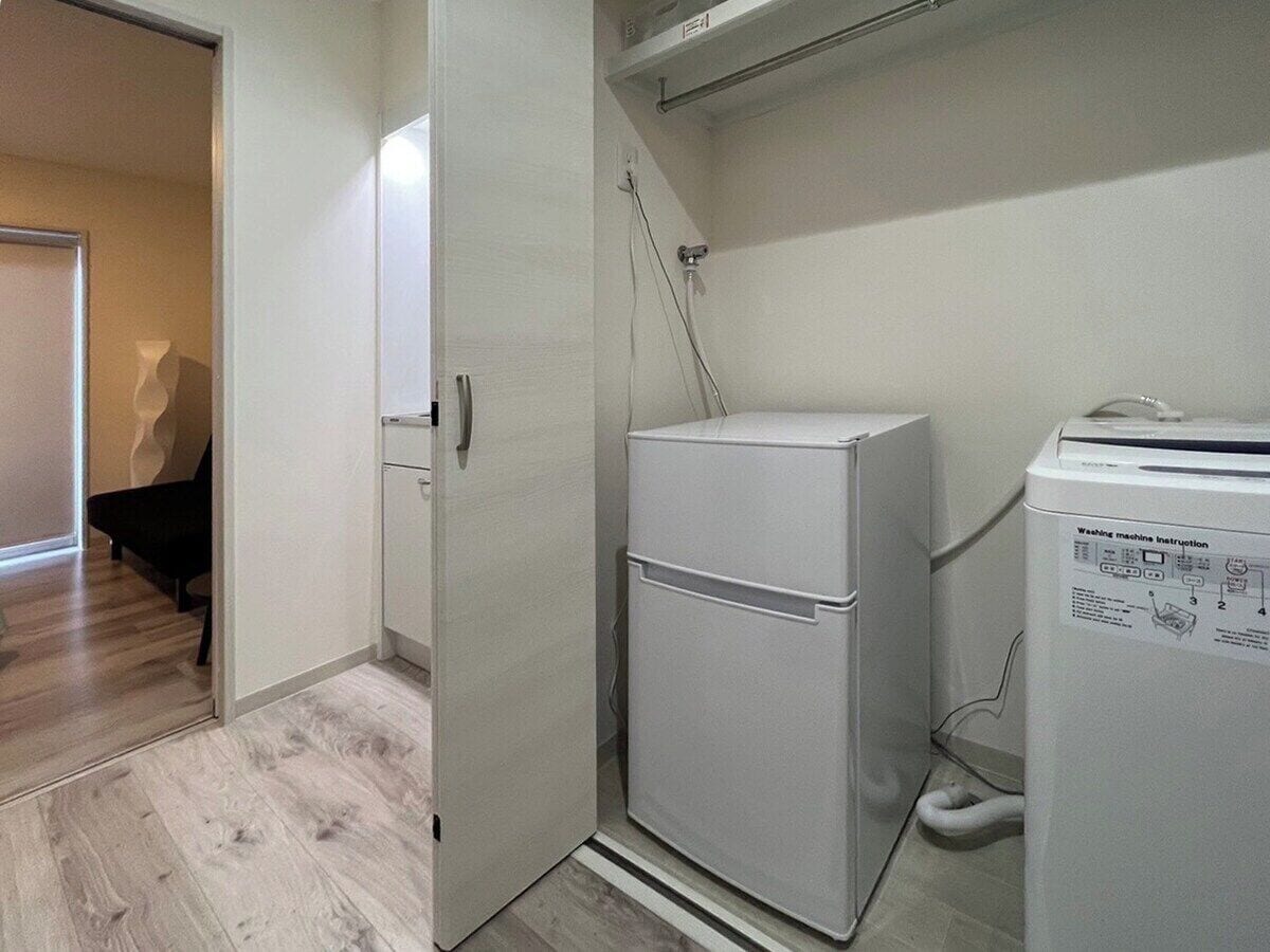 A compact laundry area with a washing machine and dryer, a door leading to a room with a piano, and a wooden floor.