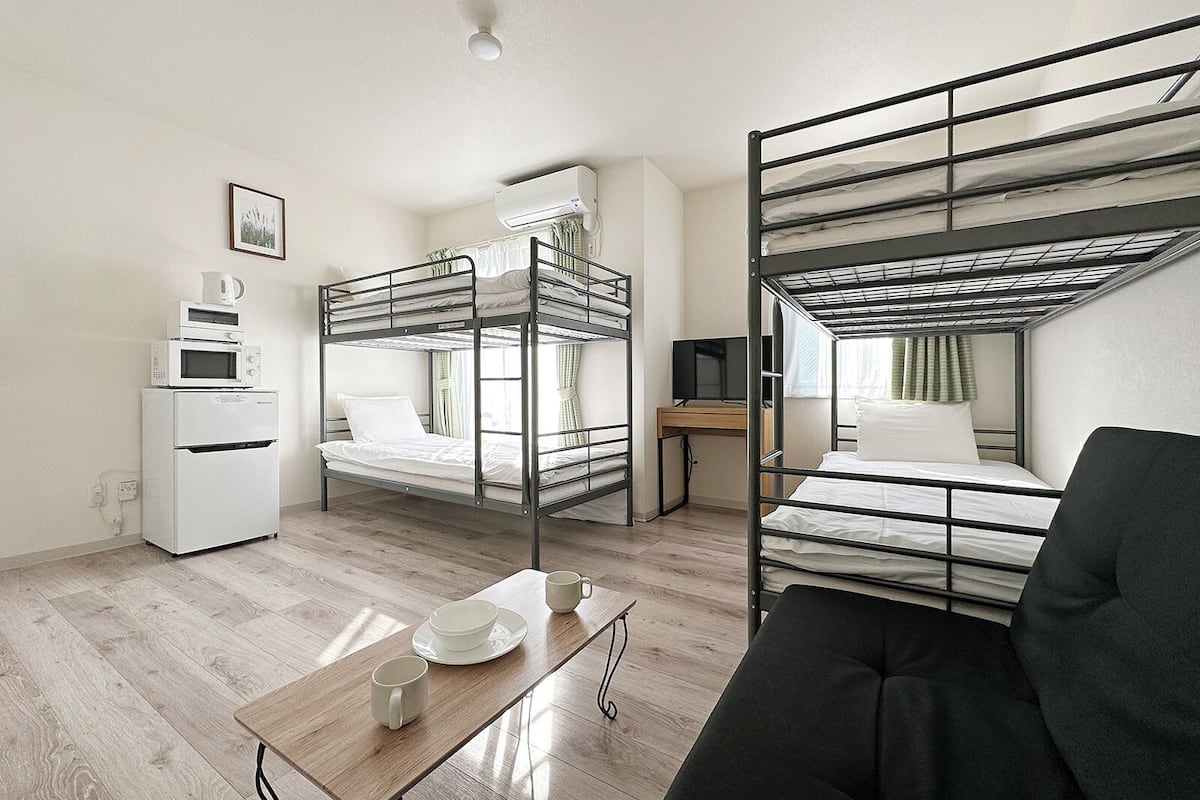 Ein Schlafsaalzimmer mit Etagenbetten, einem Schreibtisch, einer Mikrowelle, einem Kühlschrank und einem Tisch mit Tassen und einer Schüssel.
