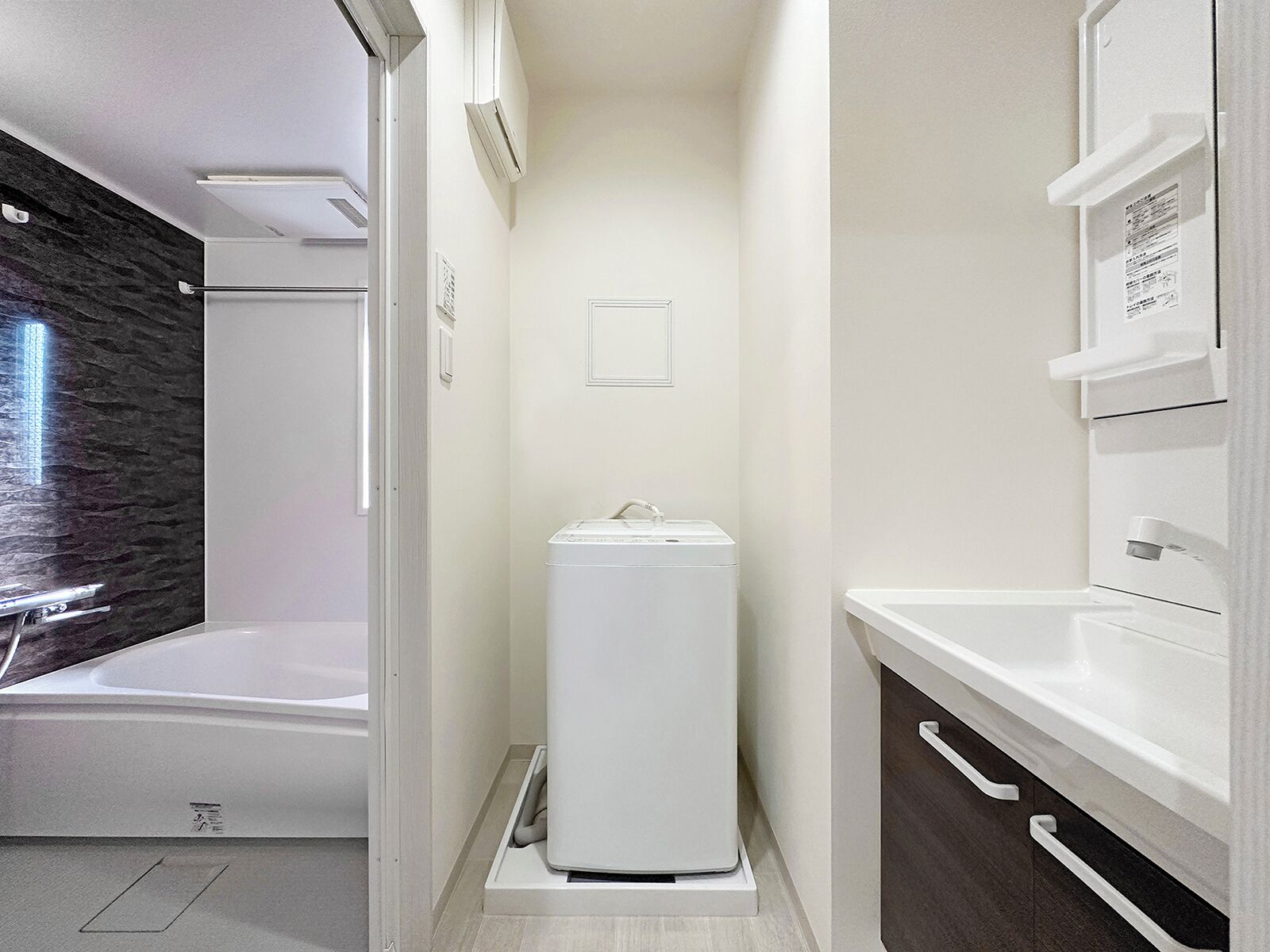 A modern bathroom with a built-in washing machine, a bathtub, and a vanity with drawers.