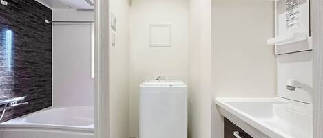 A modern bathroom with a built-in washing machine, a bathtub, and a vanity with drawers.