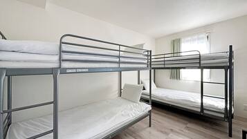 A dormitory room with bunk beds, wooden flooring, and a window with curtains.