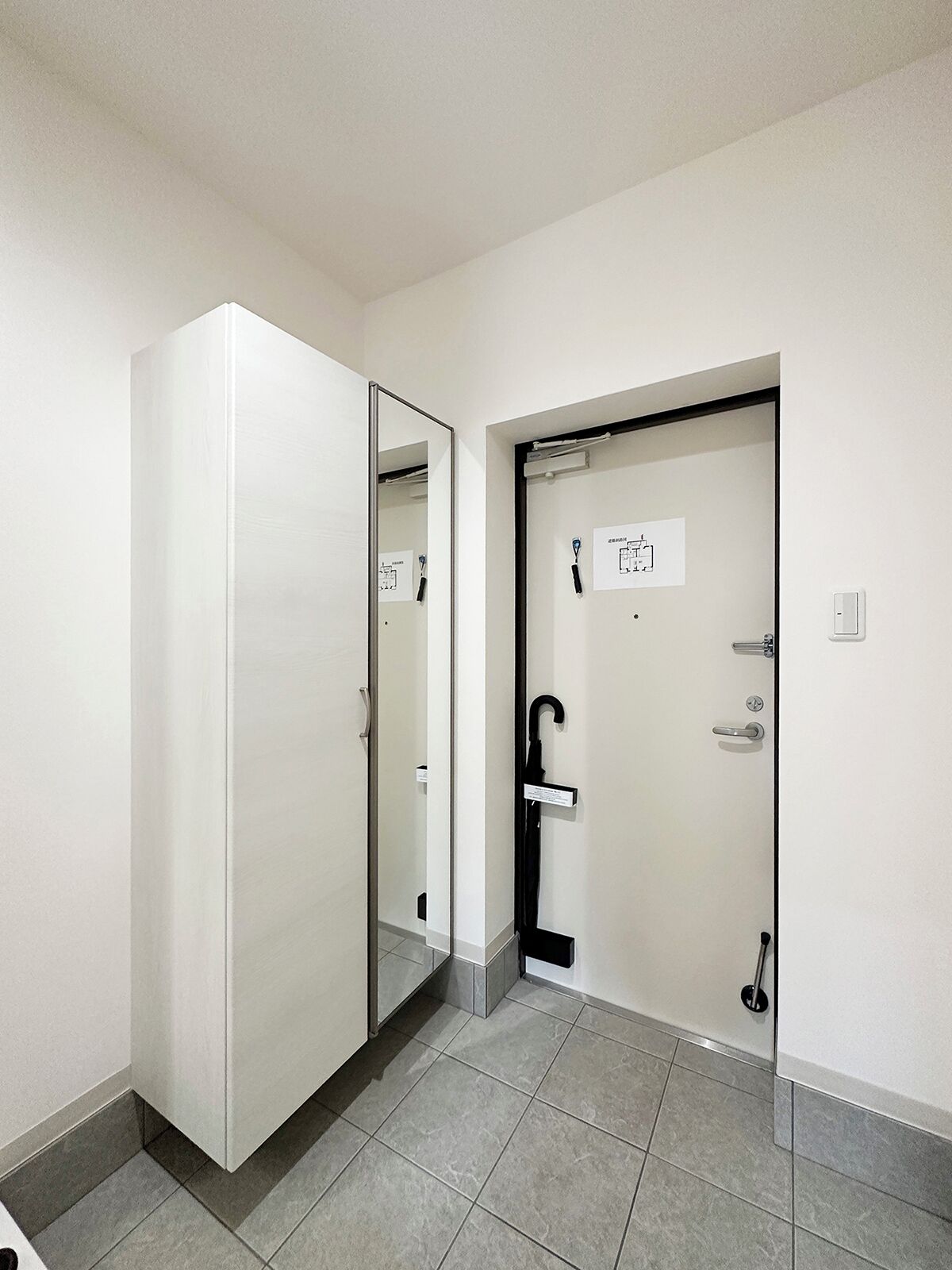 A hotel room with a large mirror, a door with a black handle, and a small sign on the door.