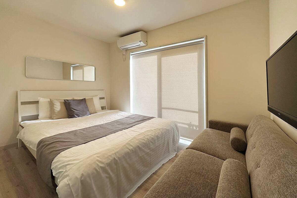 Ein Hotelzimmer mit Bett, Sofa, einem großen Spiegel, einer Klimaanlage und einer Schiebetür.