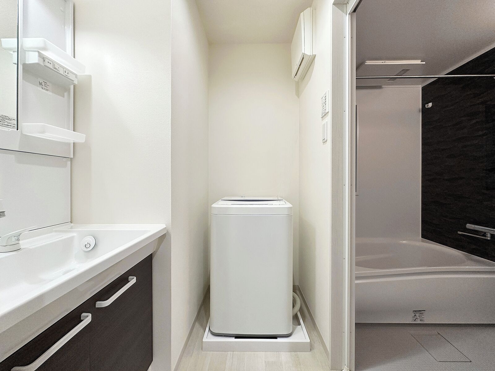 Un baño moderno con un lavamanos blanco, armarios de tonos oscuros, un toallero blanco y una zona de ducha.