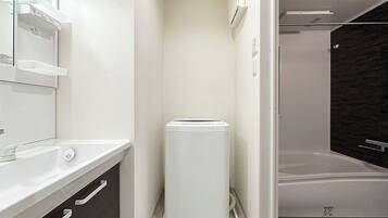 Un baño moderno con un lavamanos blanco, armarios de tonos oscuros, un toallero blanco y una zona de ducha.