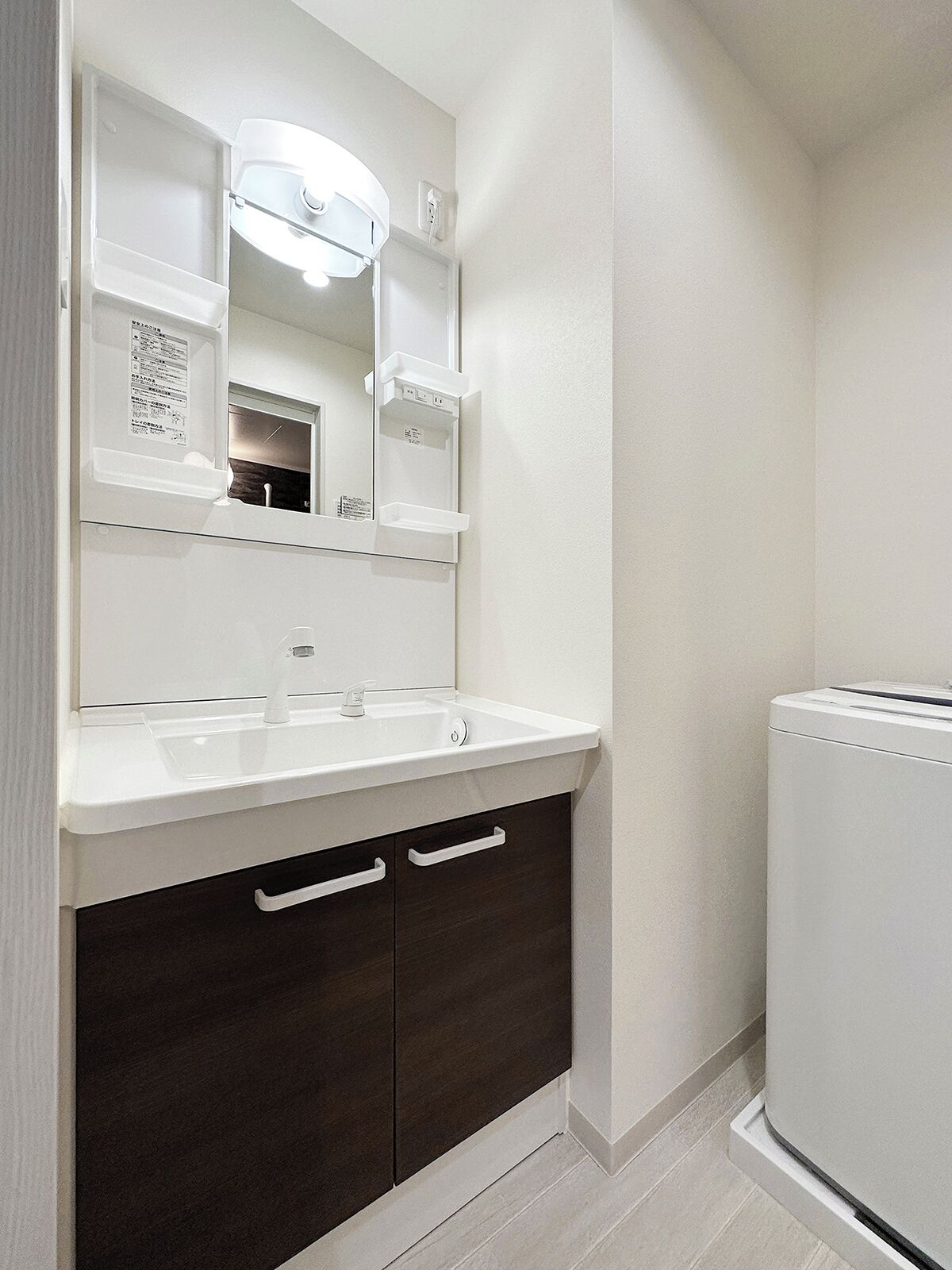 A bathroom with a white sink, dark cabinets, and a mirror with built-in lighting.