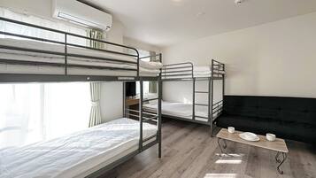 A dormitory room with bunk beds, a desk, a small table with cups, and an air conditioning unit.