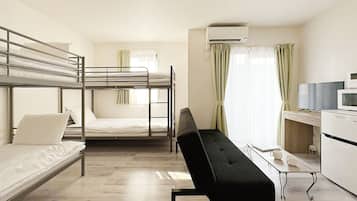 A dormitory room with bunk beds, a black sofa, a desk with a computer, and an air conditioning unit.