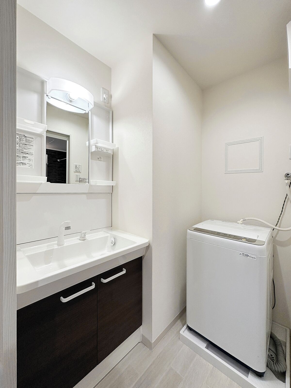 A modern bathroom with a white sink, dark cabinet, and a white washing machine.