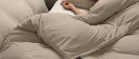 A bed with a person lying in a beige blanket.