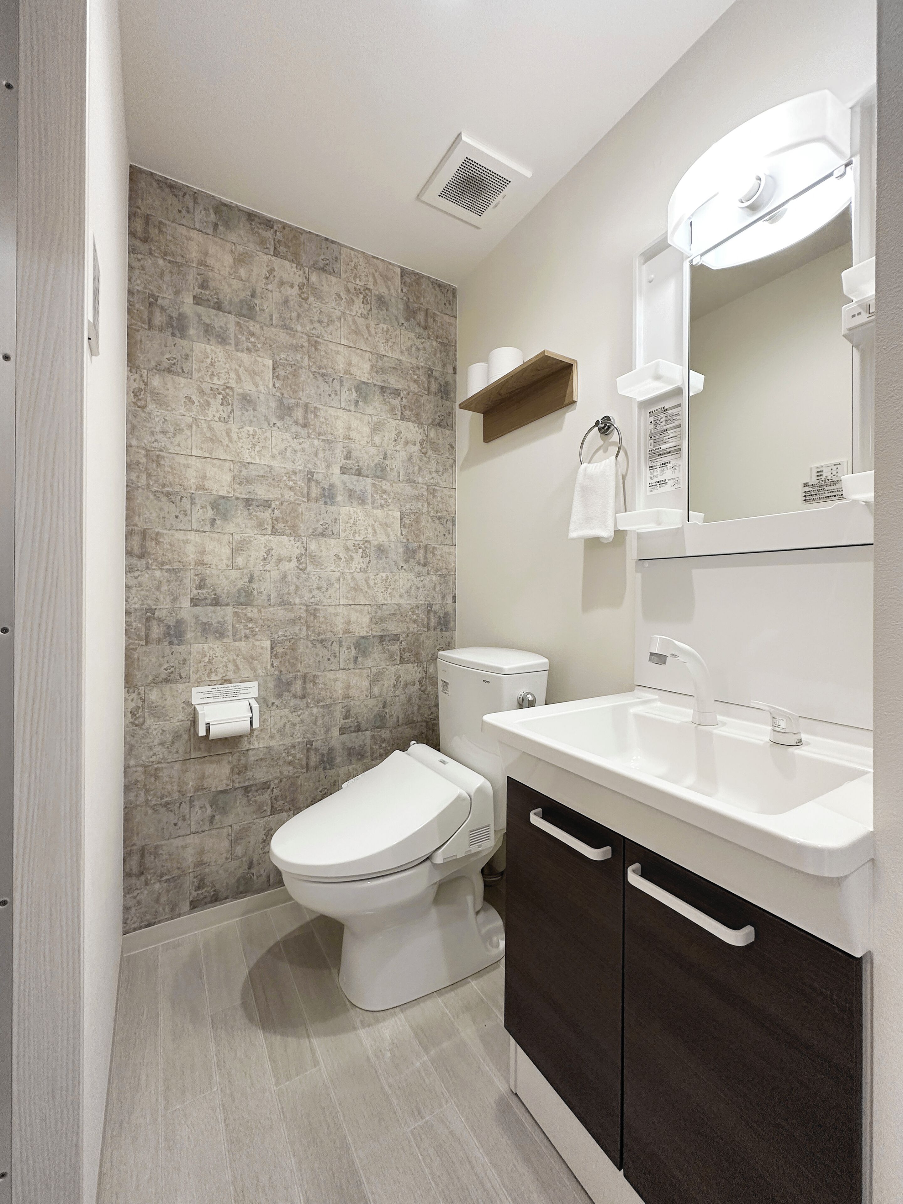 Un baño moderno con salpicadero de piedra, un inodoro, un lavamanos con espejo y un perchero para toallas.