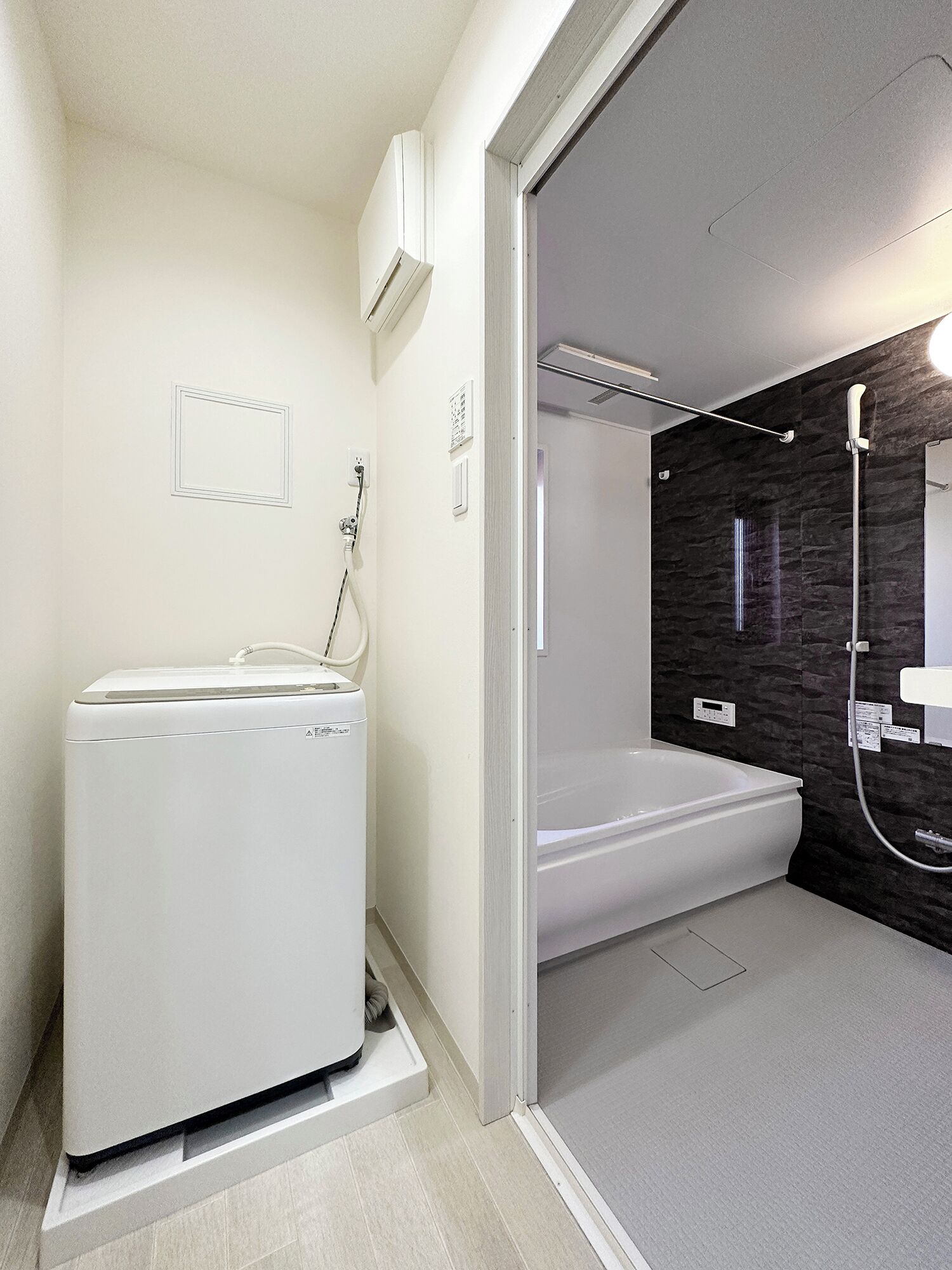 A modern bathroom with a built-in washer and dryer, a bathtub, and a shower area with a dark wall.