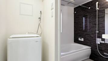 A modern bathroom with a built-in washer and dryer, a bathtub, and a shower area with a dark wall.