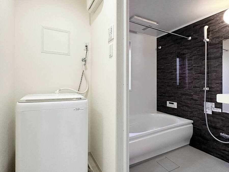 A modern bathroom with a built-in washer and dryer, a bathtub, and a shower area with a dark wall.