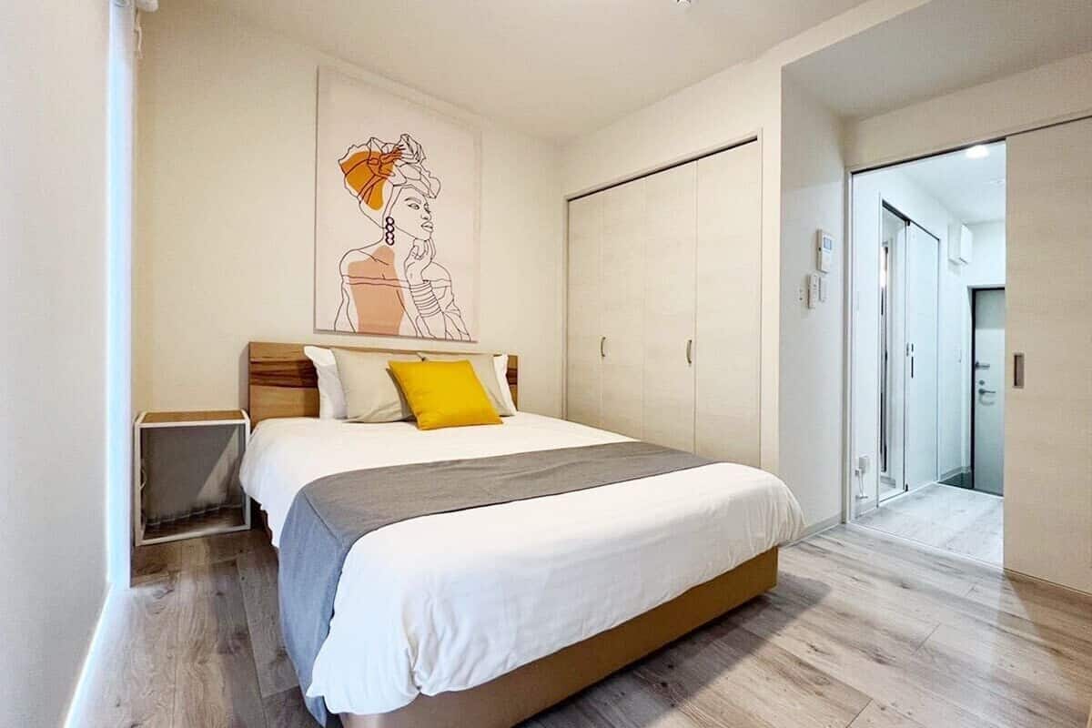 Ein modernes Schlafzimmer mit einem großen Bett, einem Nachttisch, einem Kleiderschrank und einem durchgehenden Türspalt sichtbaren Badezimmer.