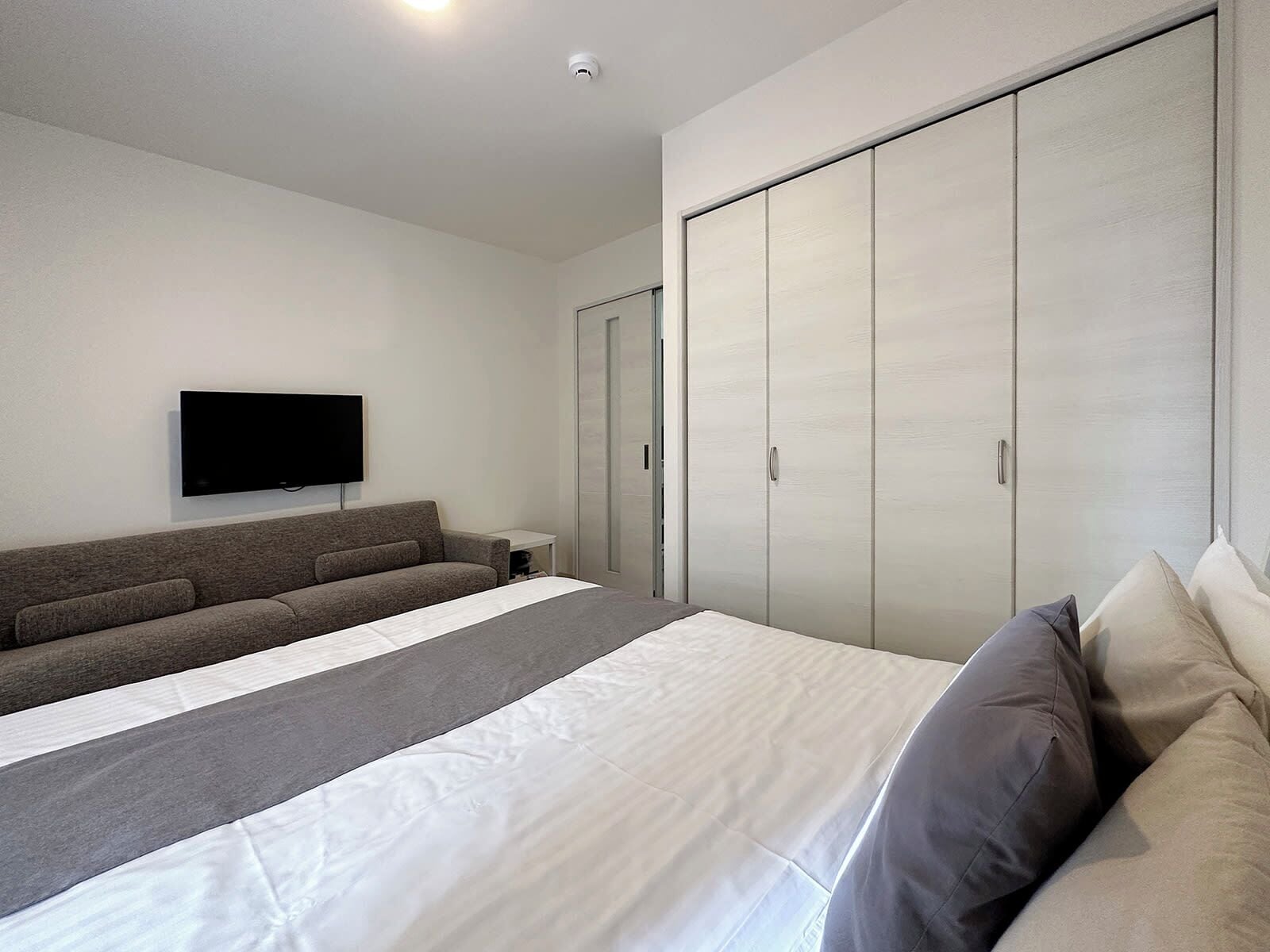 Een moderne slaapkamer met een groot bed, een bank, een televisie en een kledingkast.