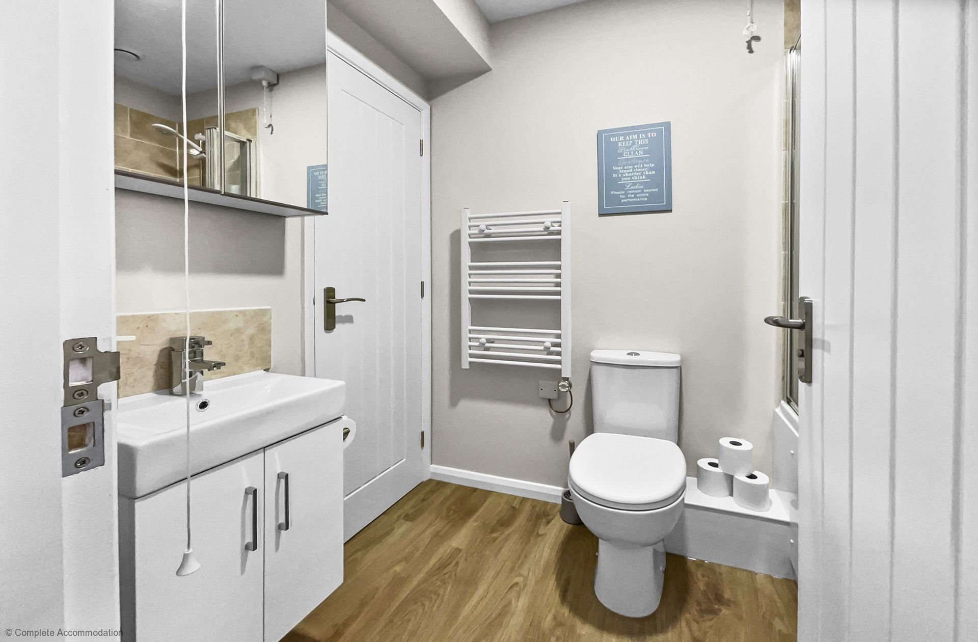 Un bagno moderno con lavandino, specchio e vaso bianco. Si nota un portasciugamani e una segnaletica a parete.
